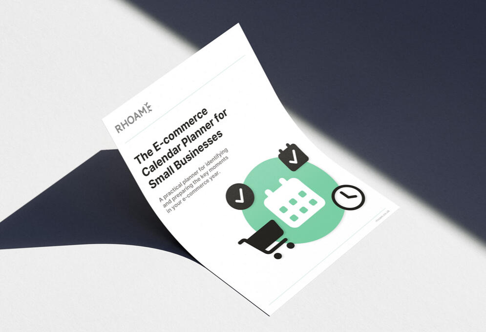 Mockup of the E-commerce Calendar Planner for Small Businesses cover placed on a desk surface, showing the Rhoam planner design with calendar, checklist, and shopping icons.